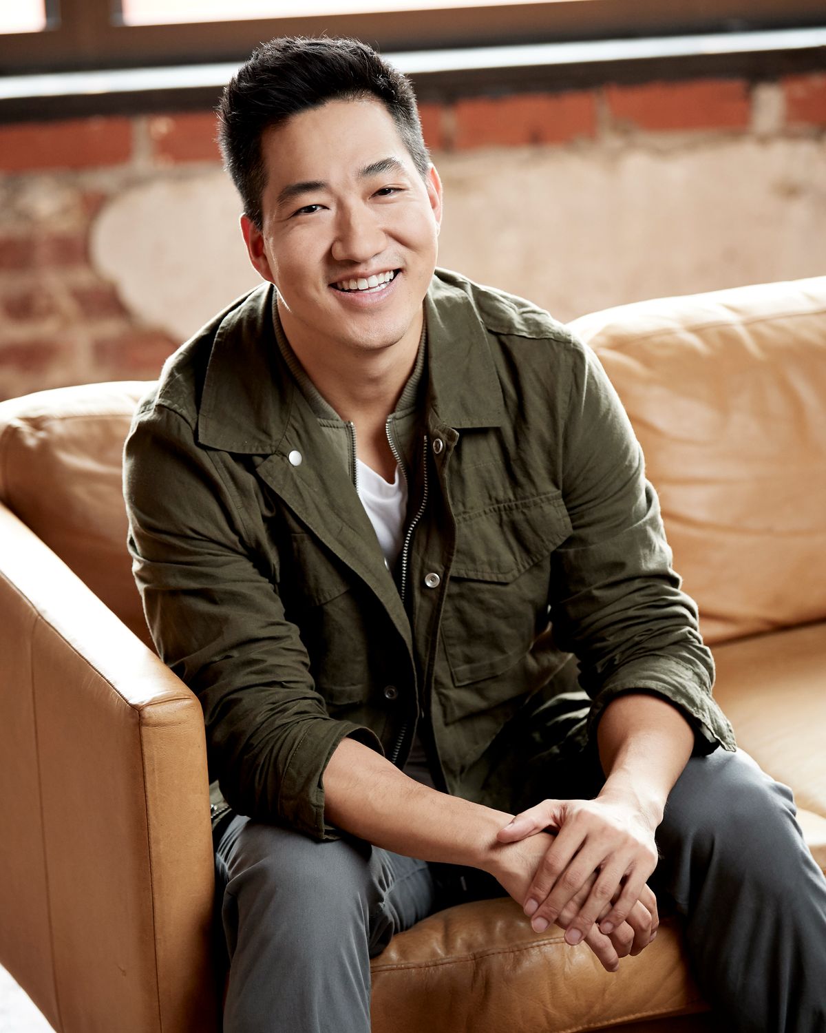 Alex Wong in a green jacket, smiling on a leather sofa