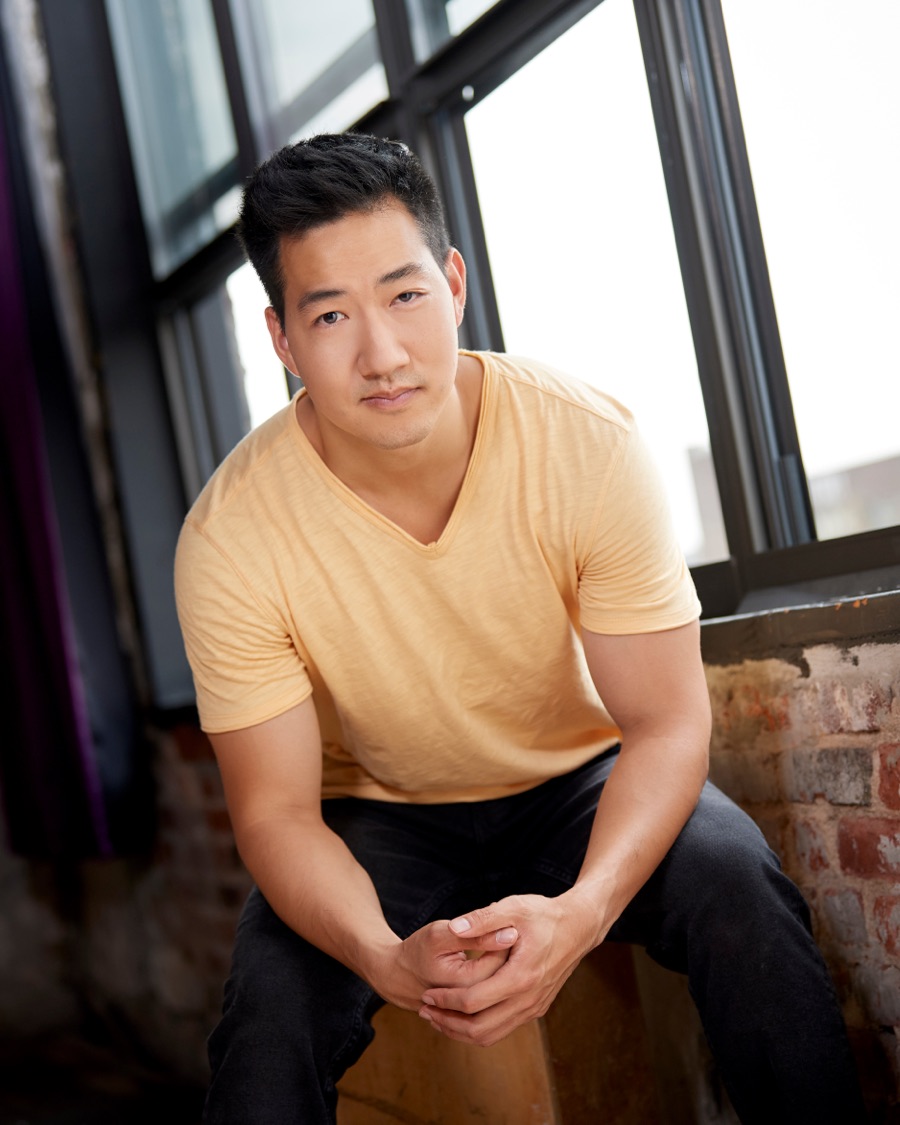 Alex Wong in a yellow T-shirt, seated on a window ledge
