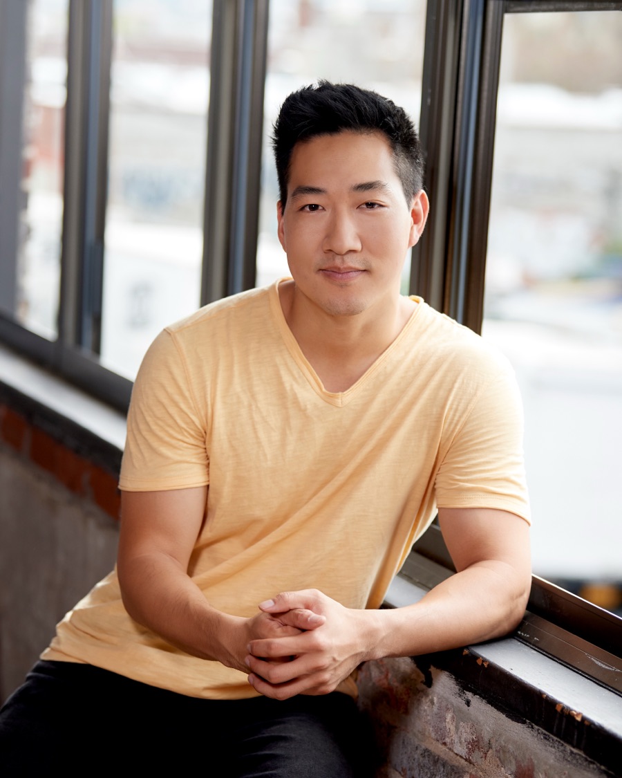 Alex Wong in a yellow T-shirt, seated by tall windows