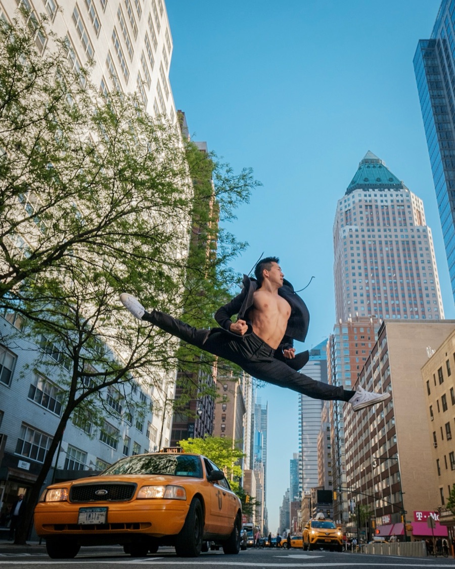 Alex Wong in a split leap above a yellow taxi under a blue sky