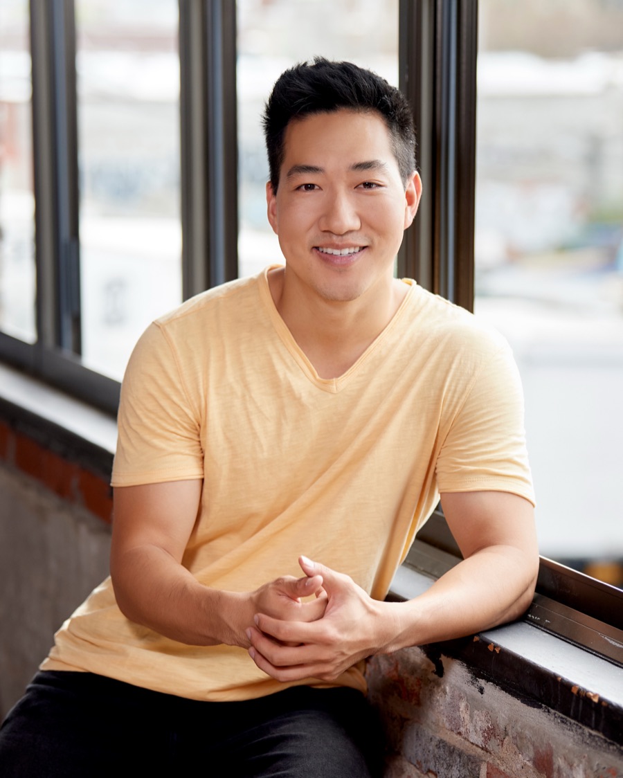 Alex Wong in a yellow T-shirt, leaning on a window ledge