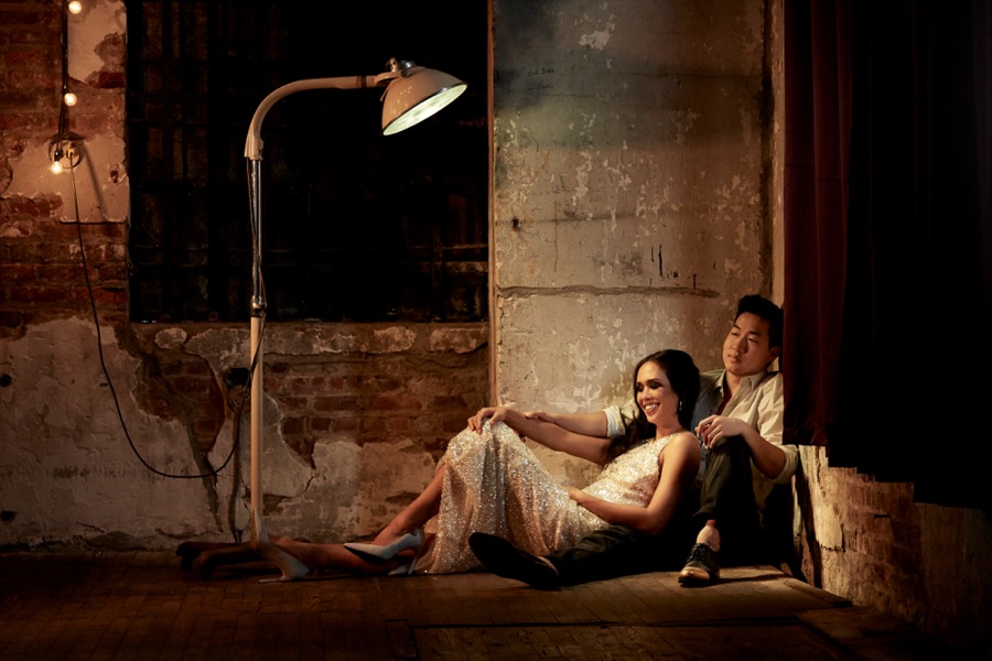 Alex Wong and a woman sitting under a lamp in a dim loft