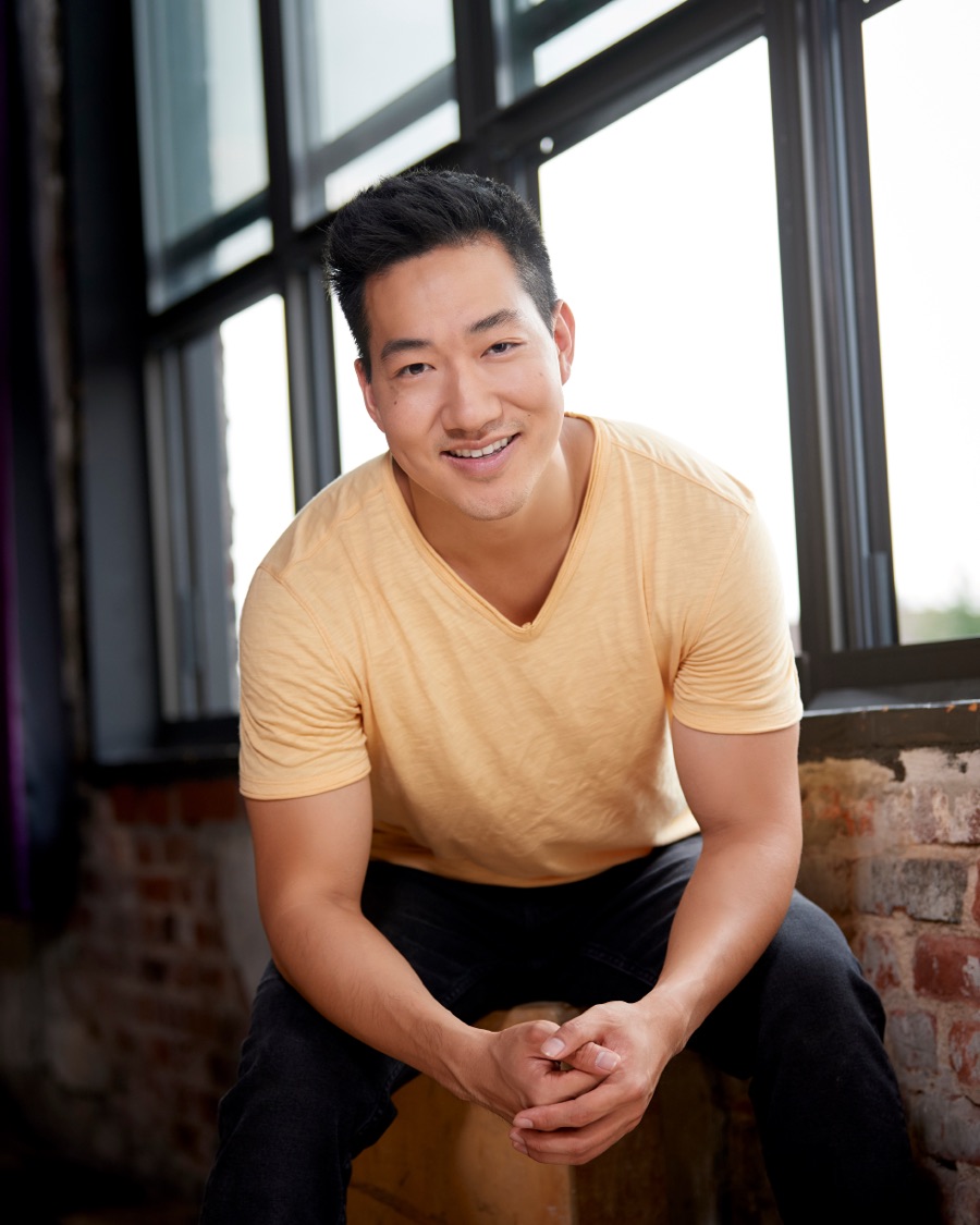 Alex Wong in a yellow T-shirt, laughing by a window