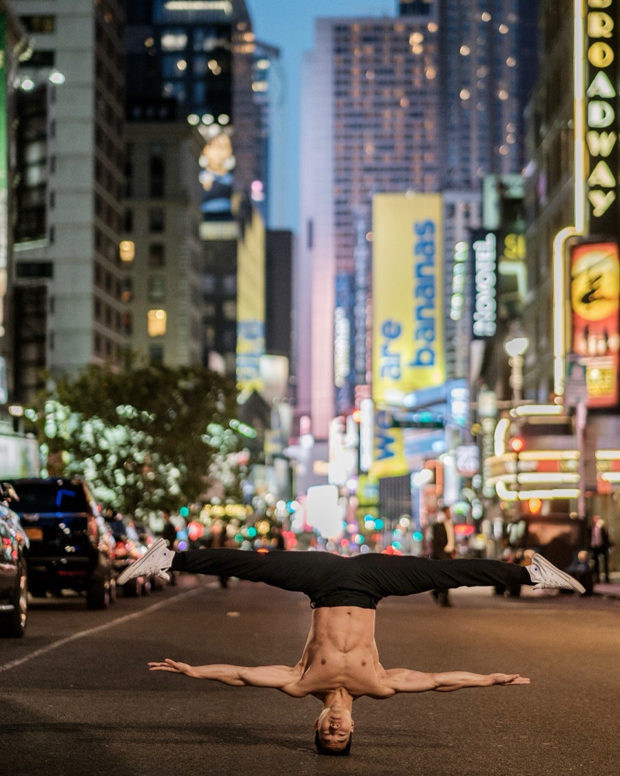 Alex Wong balancing in a headstand on a Broadway street at dusk