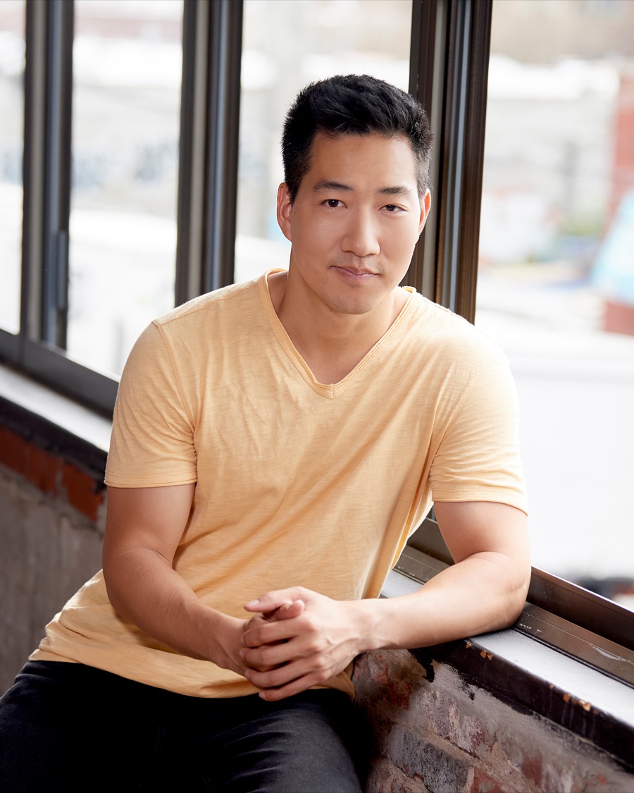 Alex Wong in a yellow T-shirt, resting his arms on a window ledge