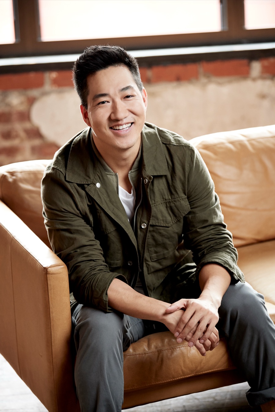 Alex Wong in a green jacket, smiling on a leather sofa