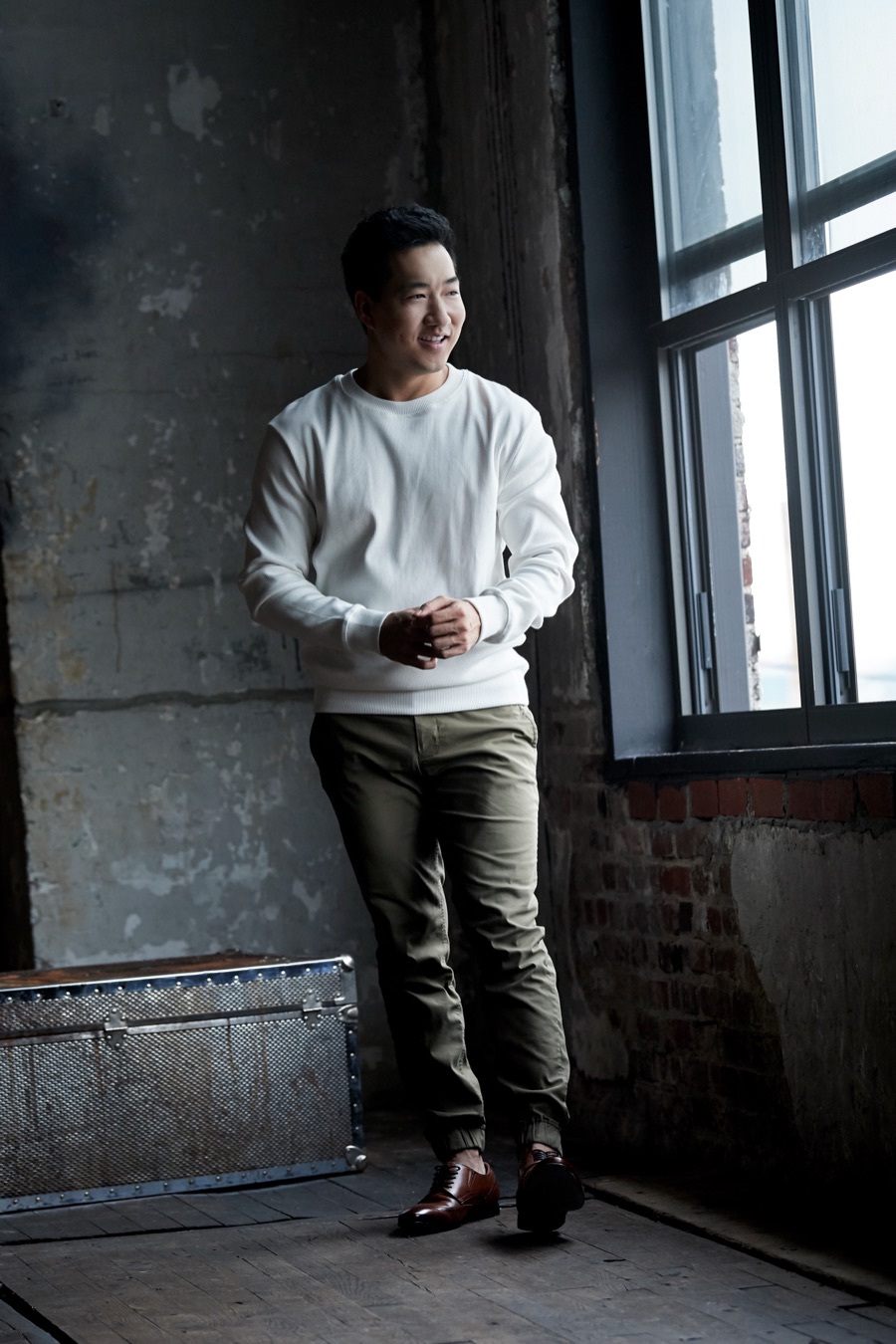 Alex Wong in a white sweater leaning by a loft window