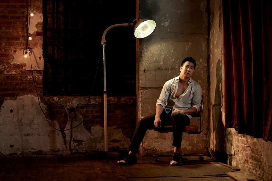 Alex Wong seated beneath a vintage lamp in a brick loft