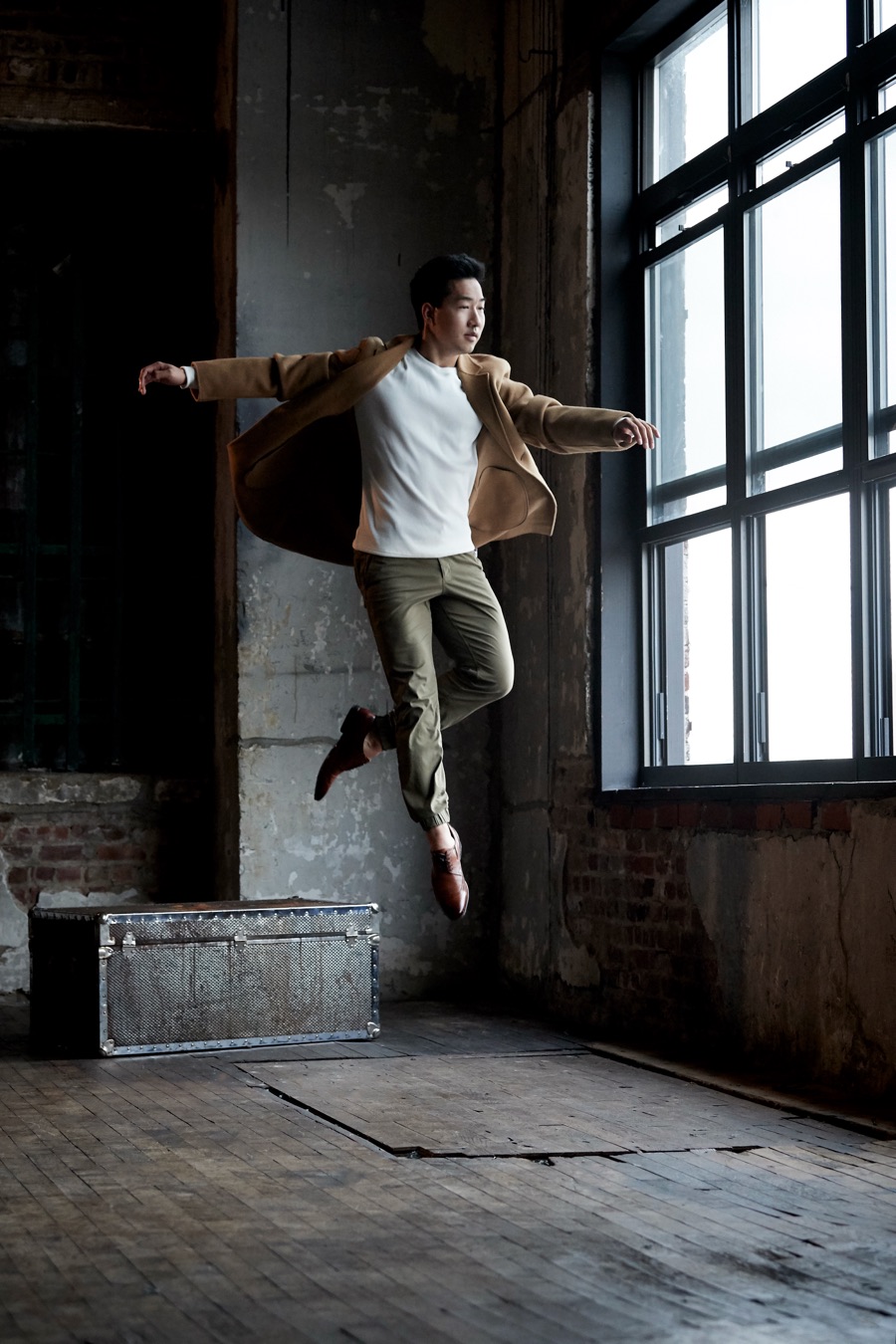 Alex Wong jumping with his jacket flying open beside tall windows